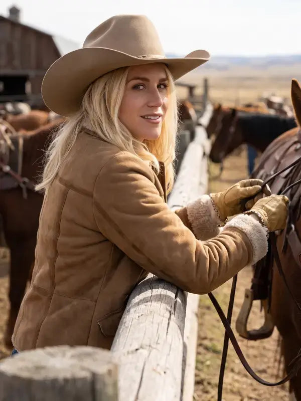 Ellyn Jameson inspired brown suede jacket side view styled with a cowboy hat beside a ranch fence