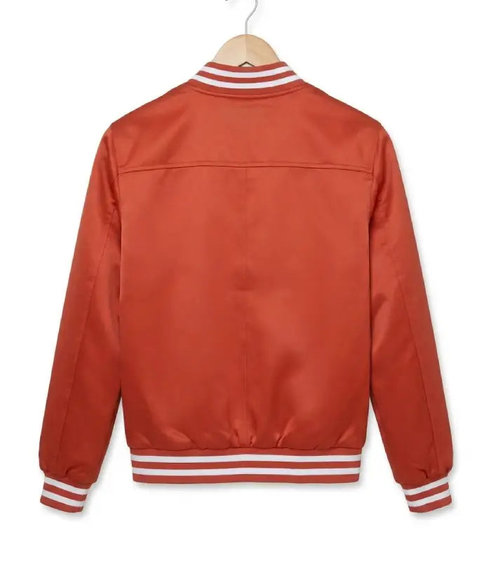 A rust-orange satin varsity jacket shown from the back, hanging on a wooden hanger against a plain white background. The jacket features white striped ribbed trim at the collar, cuffs, and hem.