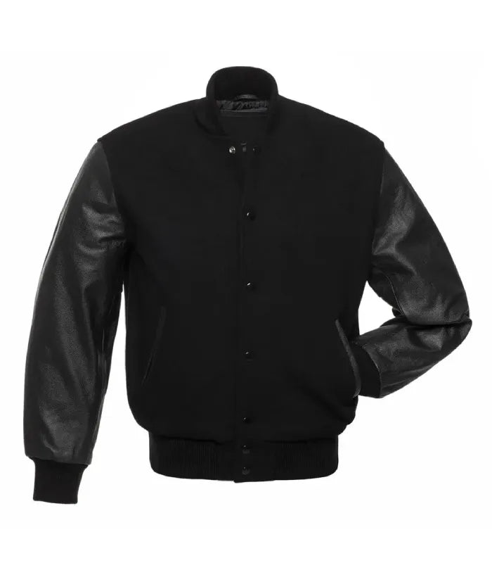 Front pose view of an all-black varsity jacket with leather sleeves, showing one hand inserted in the pocket to demonstrate fit and sleeve texture.