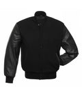 Front pose view of an all-black varsity jacket with leather sleeves, showing one hand inserted in the pocket to demonstrate fit and sleeve texture.